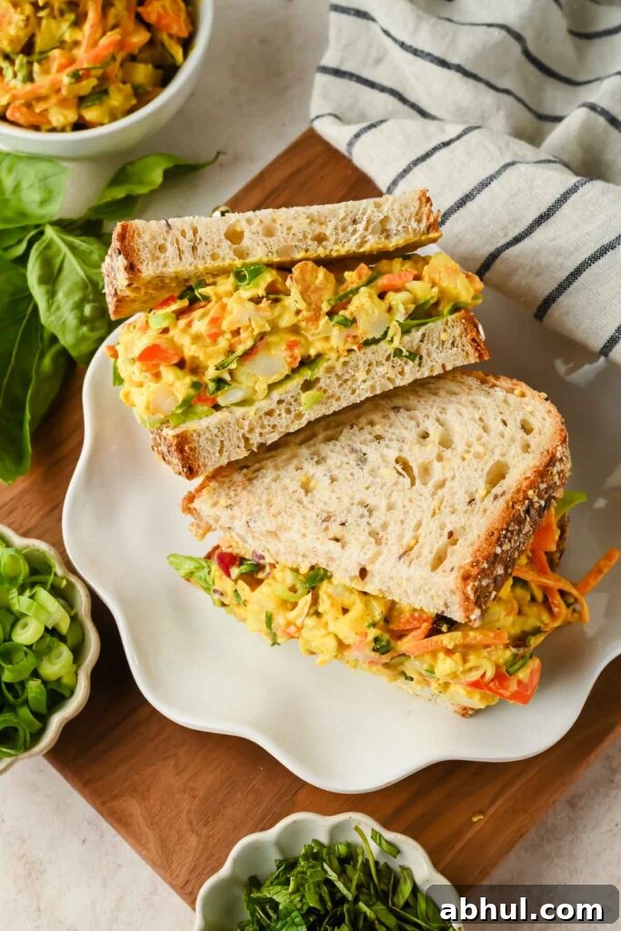two halves of shrimp curry salad sandwiches stacked on top of one another on white plate.