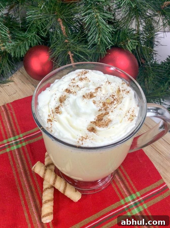 a glass mug of eggnog topped with whipped cream and ground nutmeg.