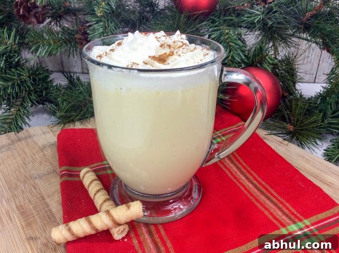 a glass mug of homemade eggnog on a red tablecloth with a Christmas tree in the background.