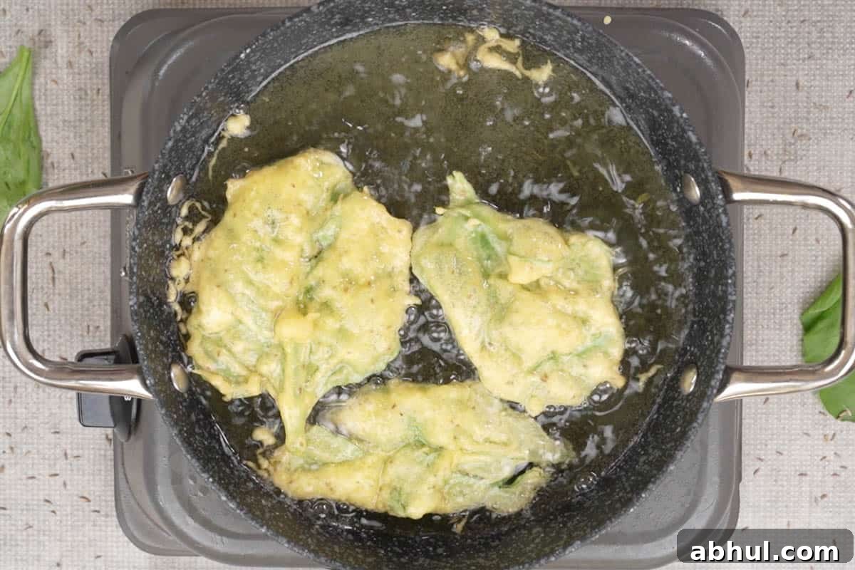 batter coated spinach leaves frying in hot oil.