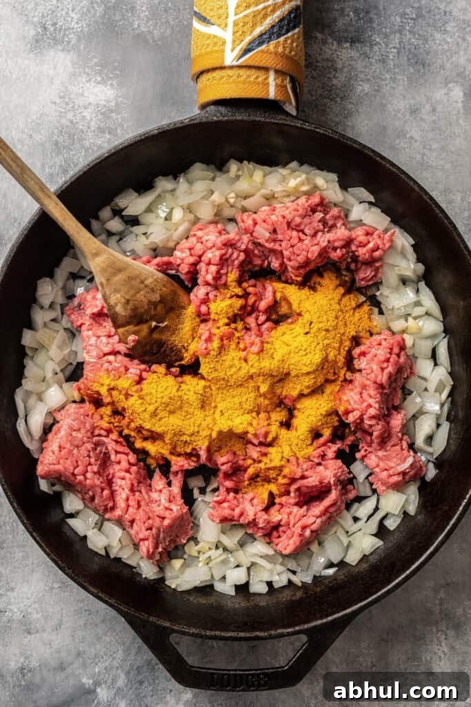 Browning ground beef with taco seasoning in a skillet with sauteed onions.