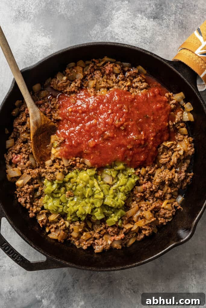 Adding salsa and canned diced green chilis to browned grownd beef in a skillet.