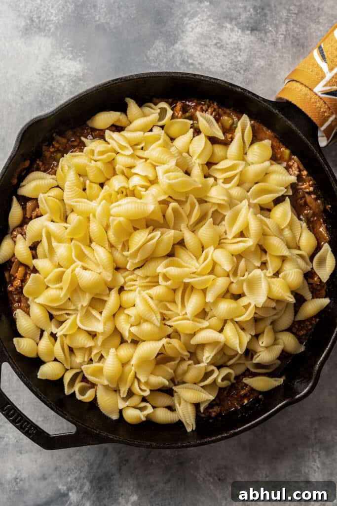 Adding cooked pasta to a skillet with sauce in it.