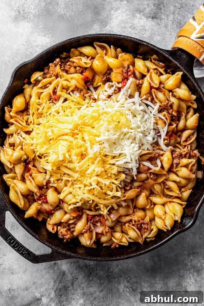Adding shredded cheese to pasta shells in a skillet.