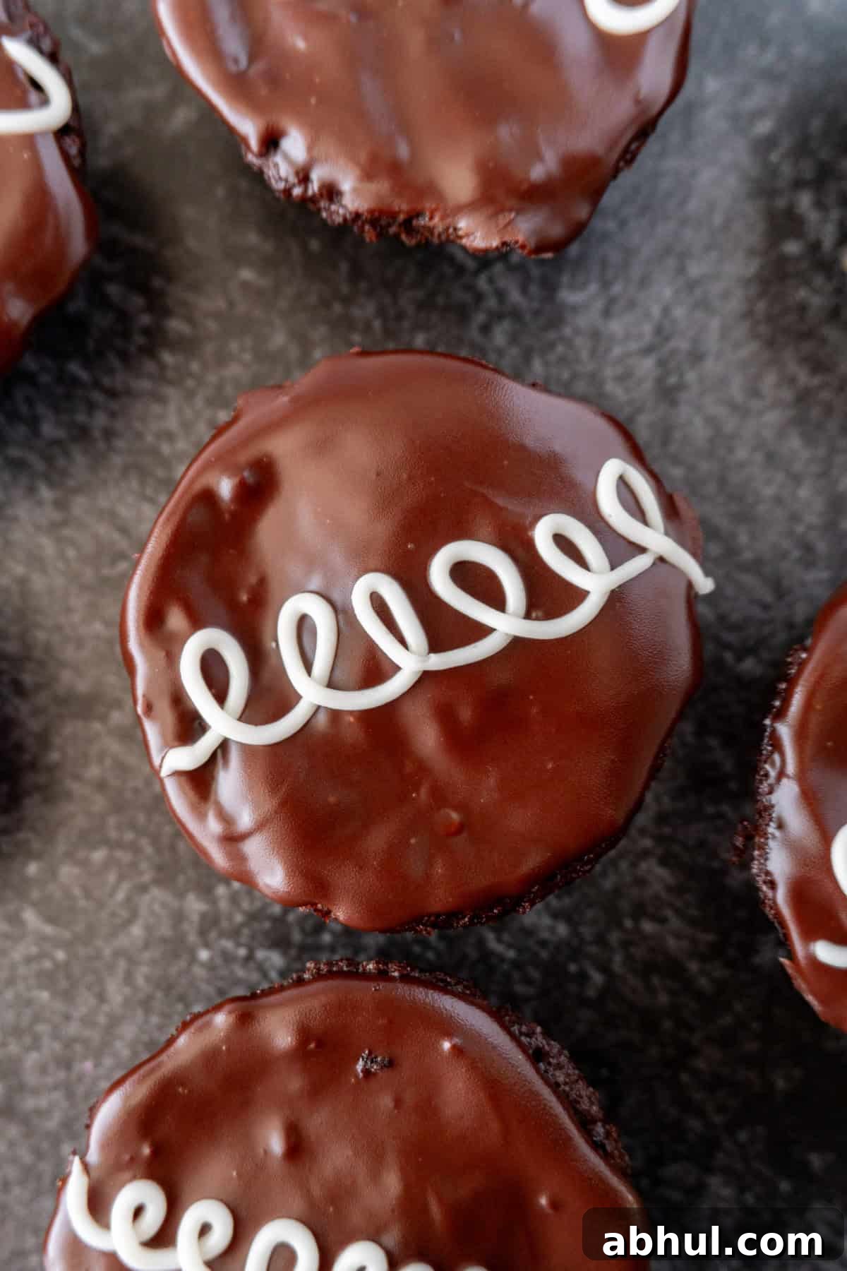 Cream Filled Chocolate cupcakes with shiny ganache topping and a line of white swirls.