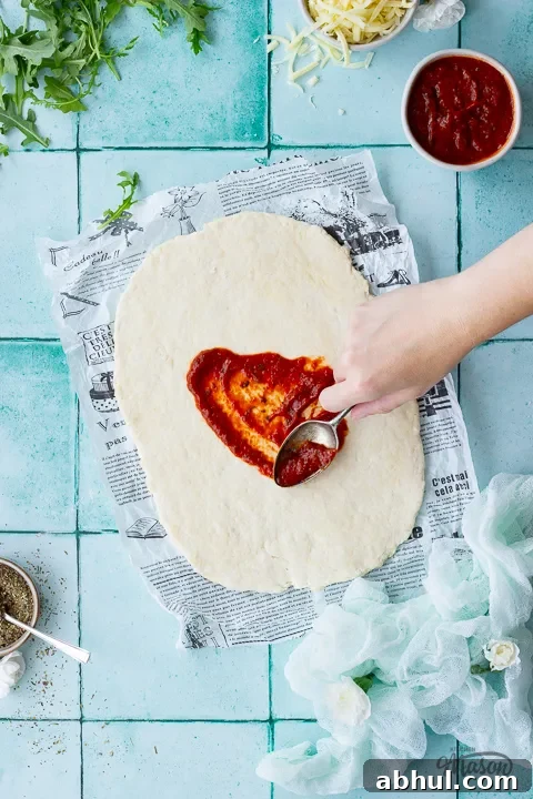 Someone spreading tomato sauce over rolled out quick pizza dough