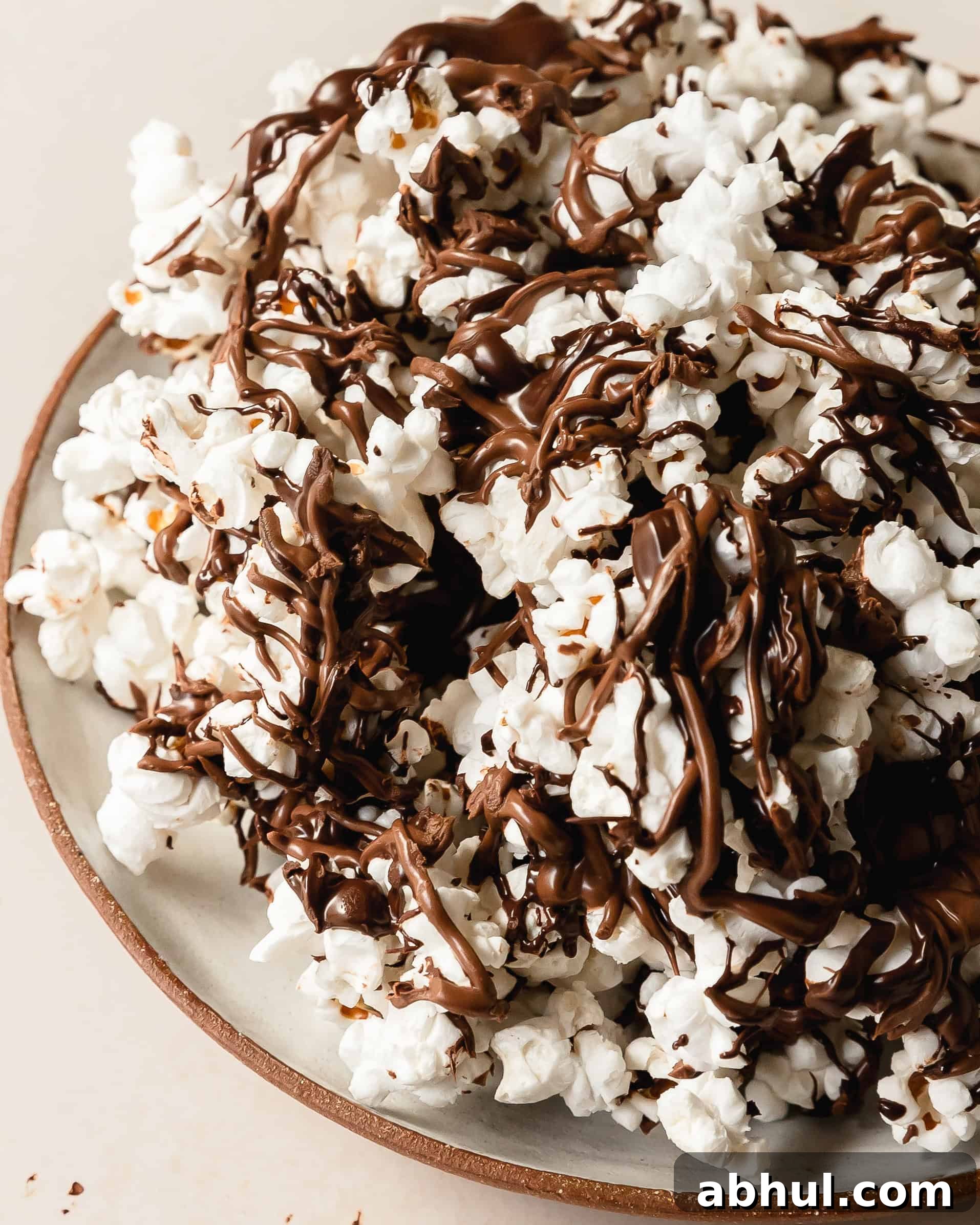 Chocolate covered popcorn is a quick, easy, salty sweet snack made with made using freshly popped popcorn topped with rich, melted chocolate drizzles. For even more flavor, top this chocolate popcorn with your favorite toppings like nuts or candy. Skip the store bought version and learn how to make these chocolate drizzled popcorn in a few easy steps.