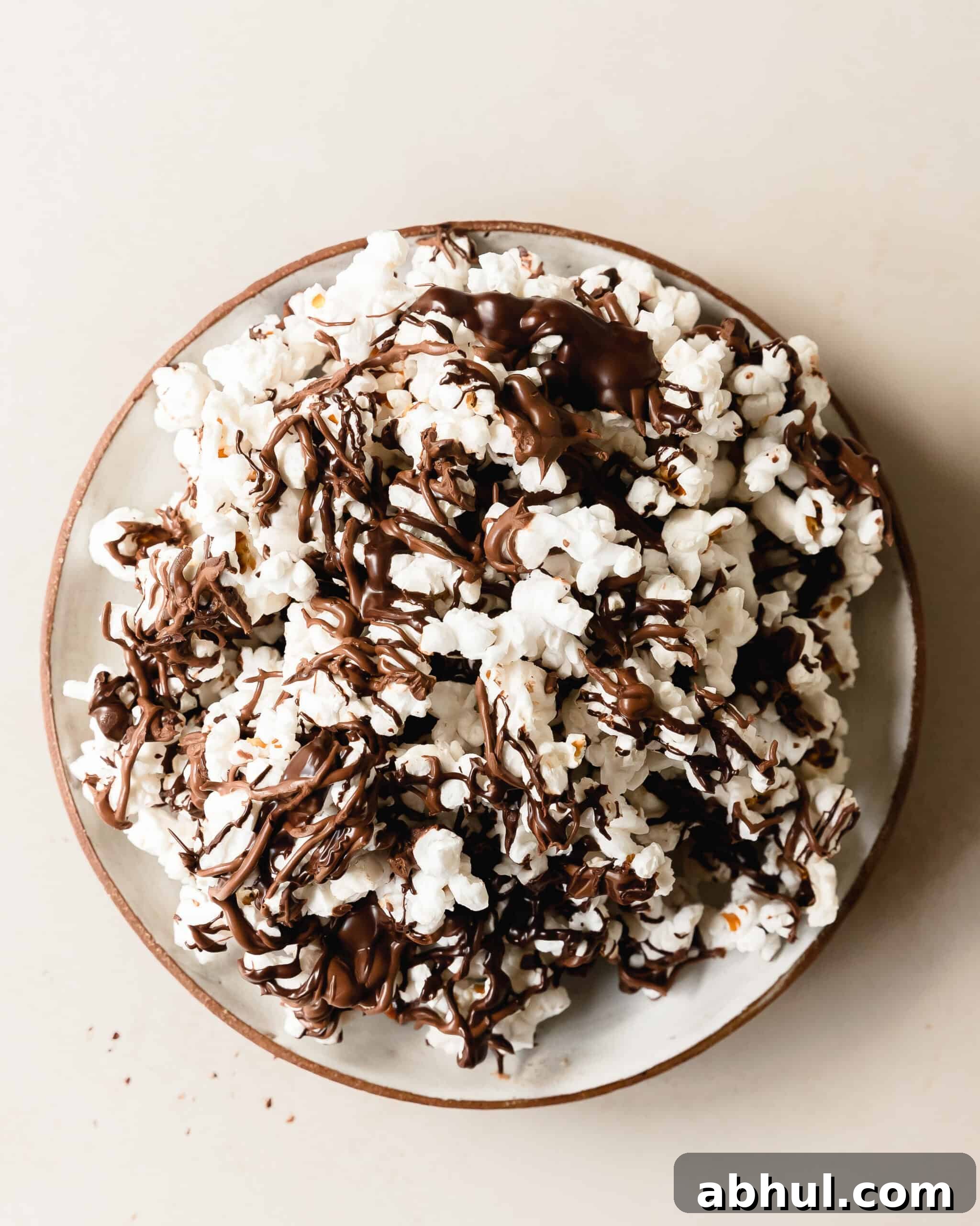 Chocolate covered popcorn is a quick, easy, salty sweet snack made with made using freshly popped popcorn topped with rich, melted chocolate drizzles. For even more flavor, top this chocolate popcorn with your favorite toppings like nuts or candy. Skip the store bought version and learn how to make these chocolate drizzled popcorn in a few easy steps.