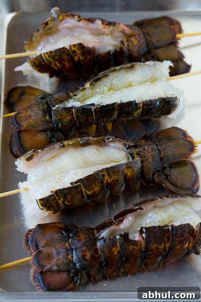 Raw lobster tails split open with skewers through them.