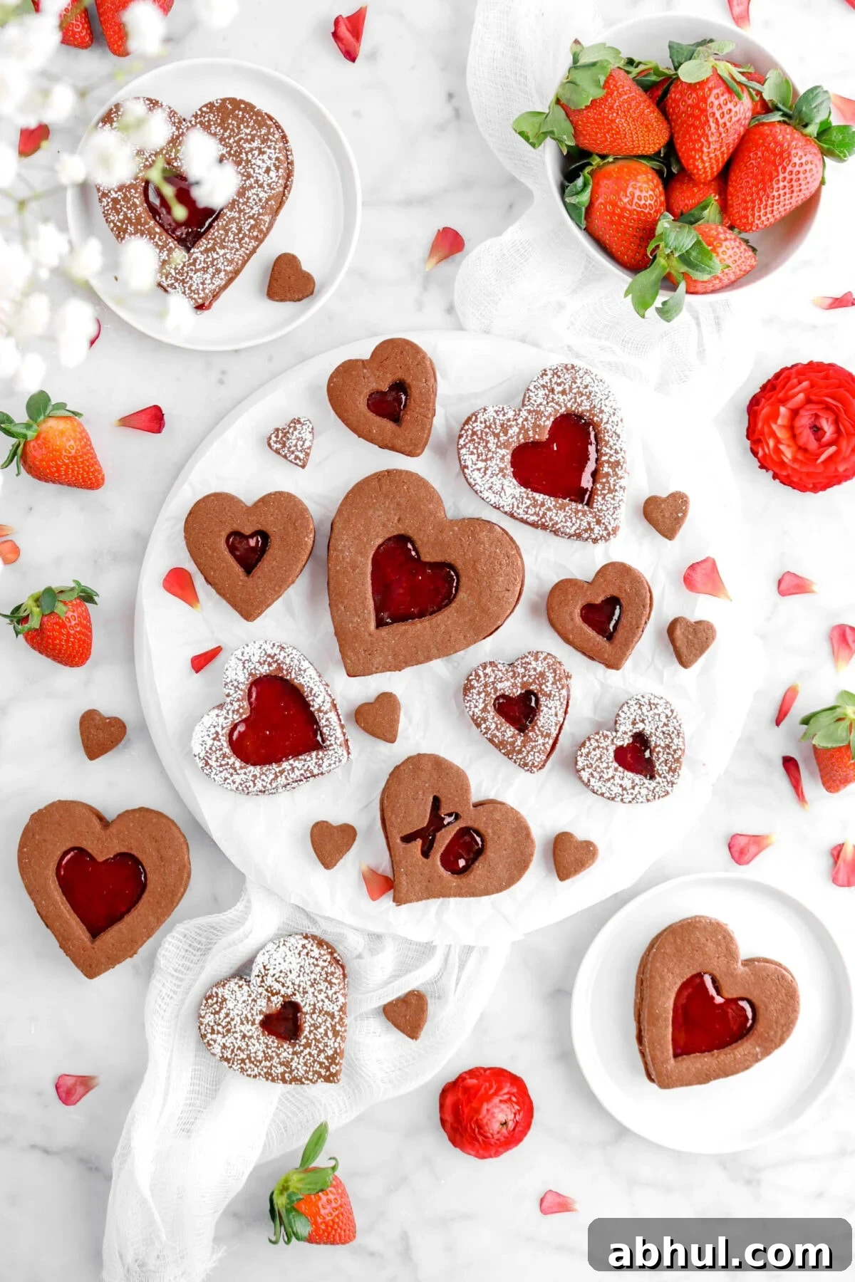 Chocolate-Strawberry Linzer Cookie Recipe for Perfect Sandwich Cookies 2 flat lay of chocolate linzer cookies with strawberry filling, fresh strawberries, red flowers, and white cheese cloth