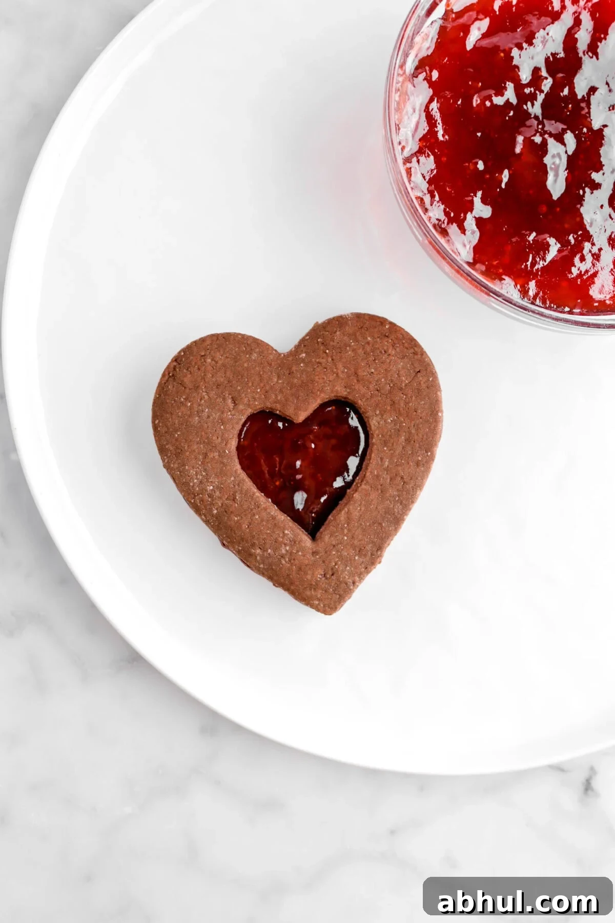 Chocolate-Strawberry Linzer Cookie Recipe for Perfect Sandwich Cookies 25 chocolate linzer cookie on white plate with bowl of strawberry jam beside