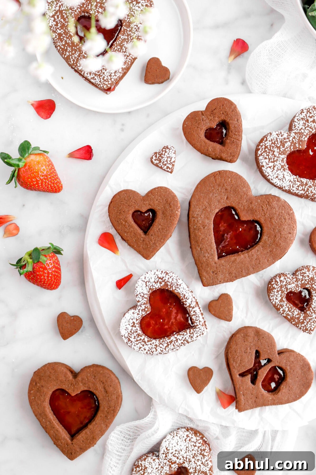 Chocolate-Strawberry Linzer Cookie Recipe for Perfect Sandwich Cookies 26 flat lay of chocolate linzer cookies on on parchment paper with red petals and white flowers