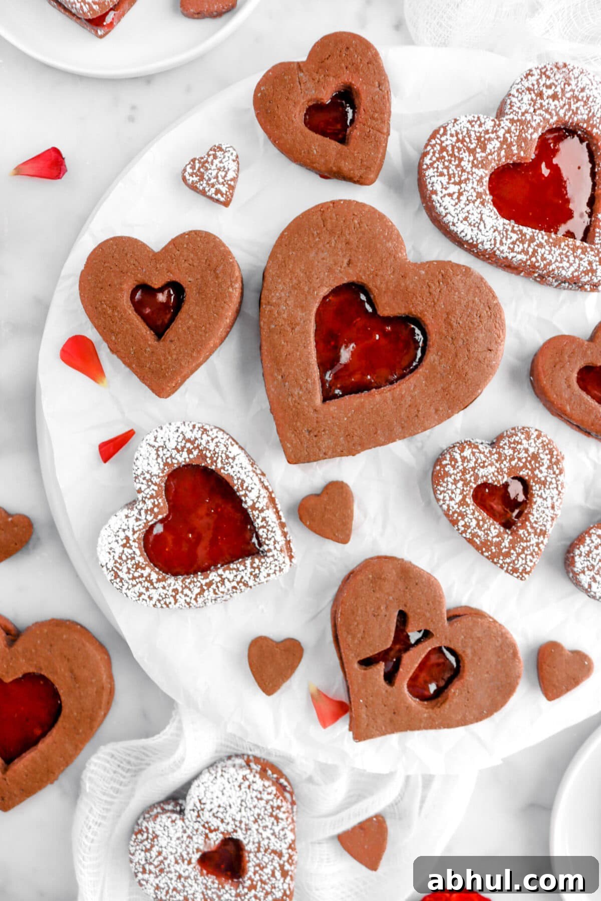 Chocolate-Strawberry Linzer Cookie Recipe for Perfect Sandwich Cookies 5 close up overhead shot if heart shaped chocolate linzer cookies on white plate