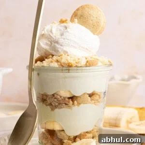 a banana pudding cup with a spoon rested against the side on a plate