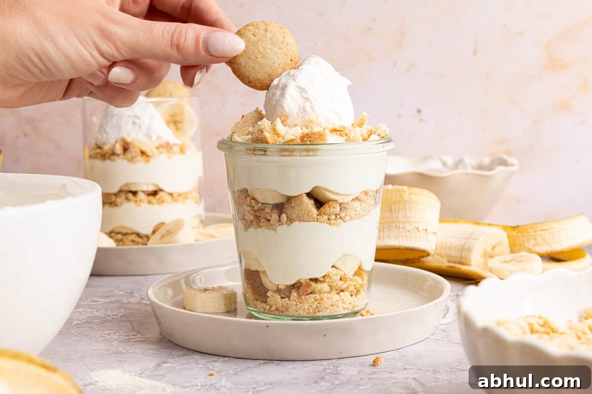 a hand placing a vanilla wafer on top of a cup of banana pudding