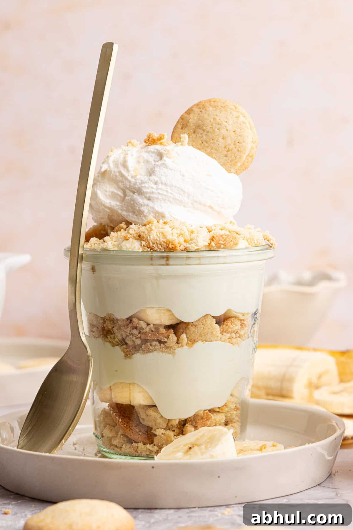 a banana pudding cup with a spoon rested against the side on a plate