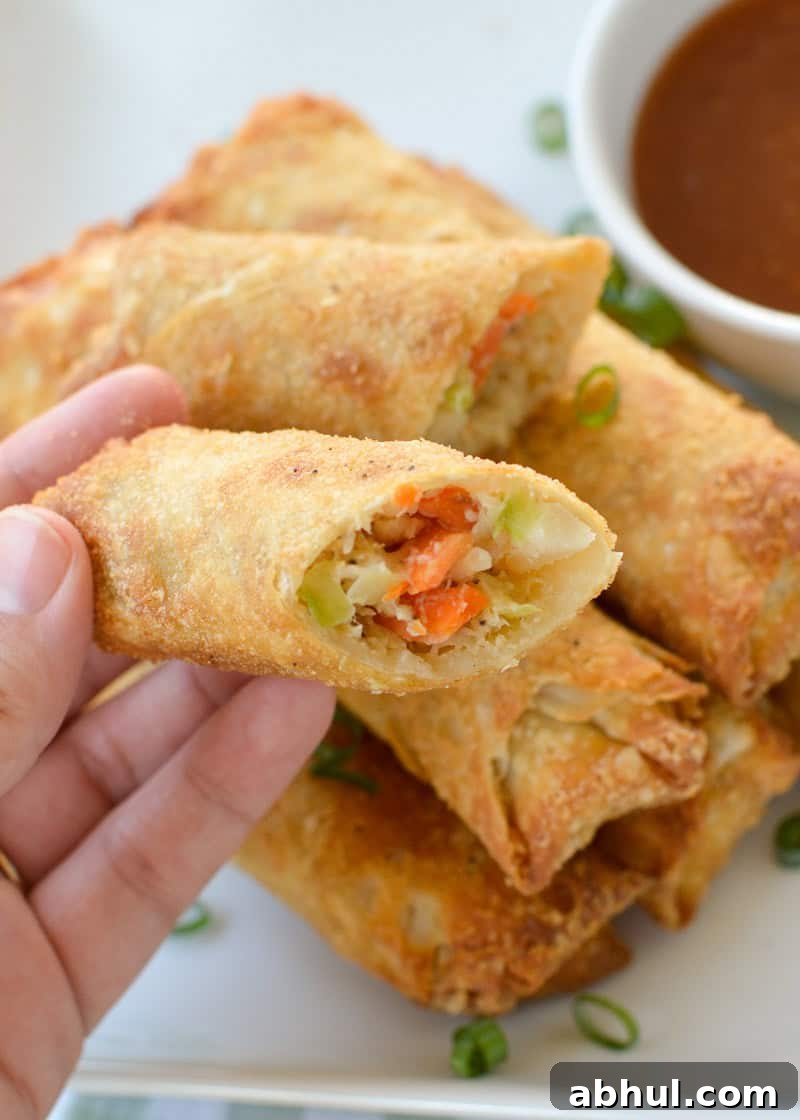 Crispy Air-Fried Egg Rolls: Quick Recipe for Homemade Crunch 7 a stack of crispy egg rolls beside a cup of dip; a hand holding a cut egg roll showing the inside filling.