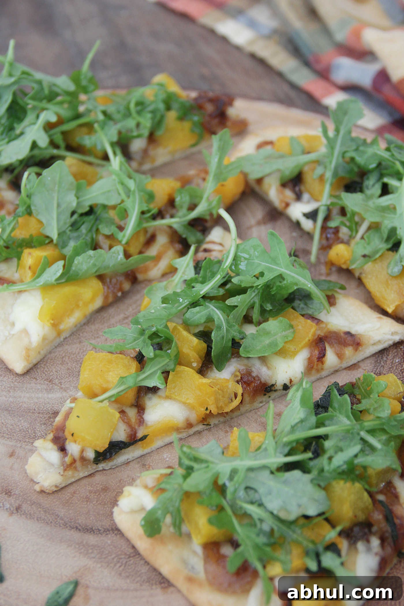 slices of flatbread pizza topped with butternut squash, caramelized onion, and arugula on a wooden board