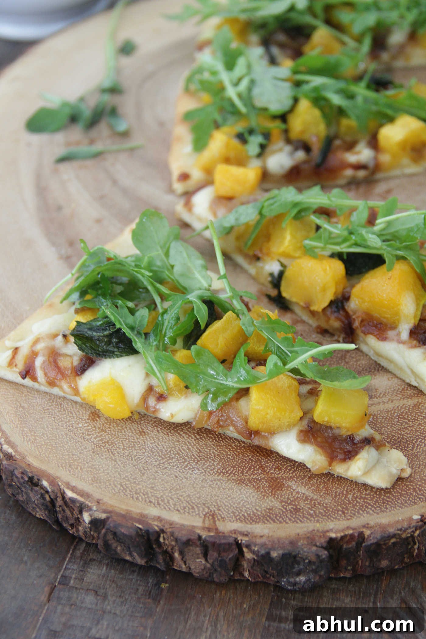 Flatbread pizza topped with cubed butternut squash, onions, and fresh arugula