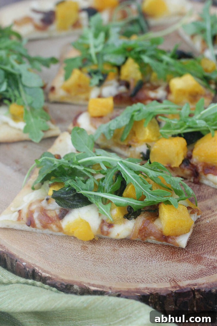 Slices of butternut squash and caramelized onions on a wooden board topped with arugula.