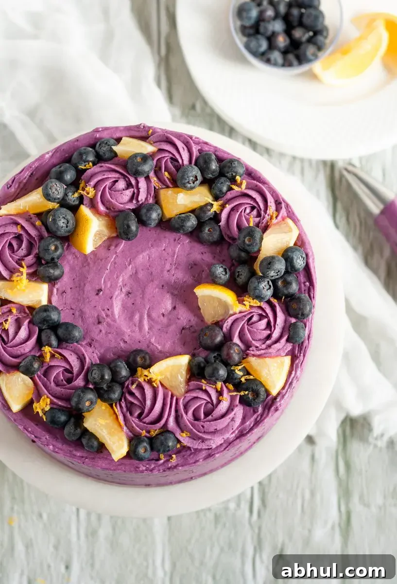 A purple lemon blueberry cake top covered in frosting swirls, lemon slices, and blueberries.