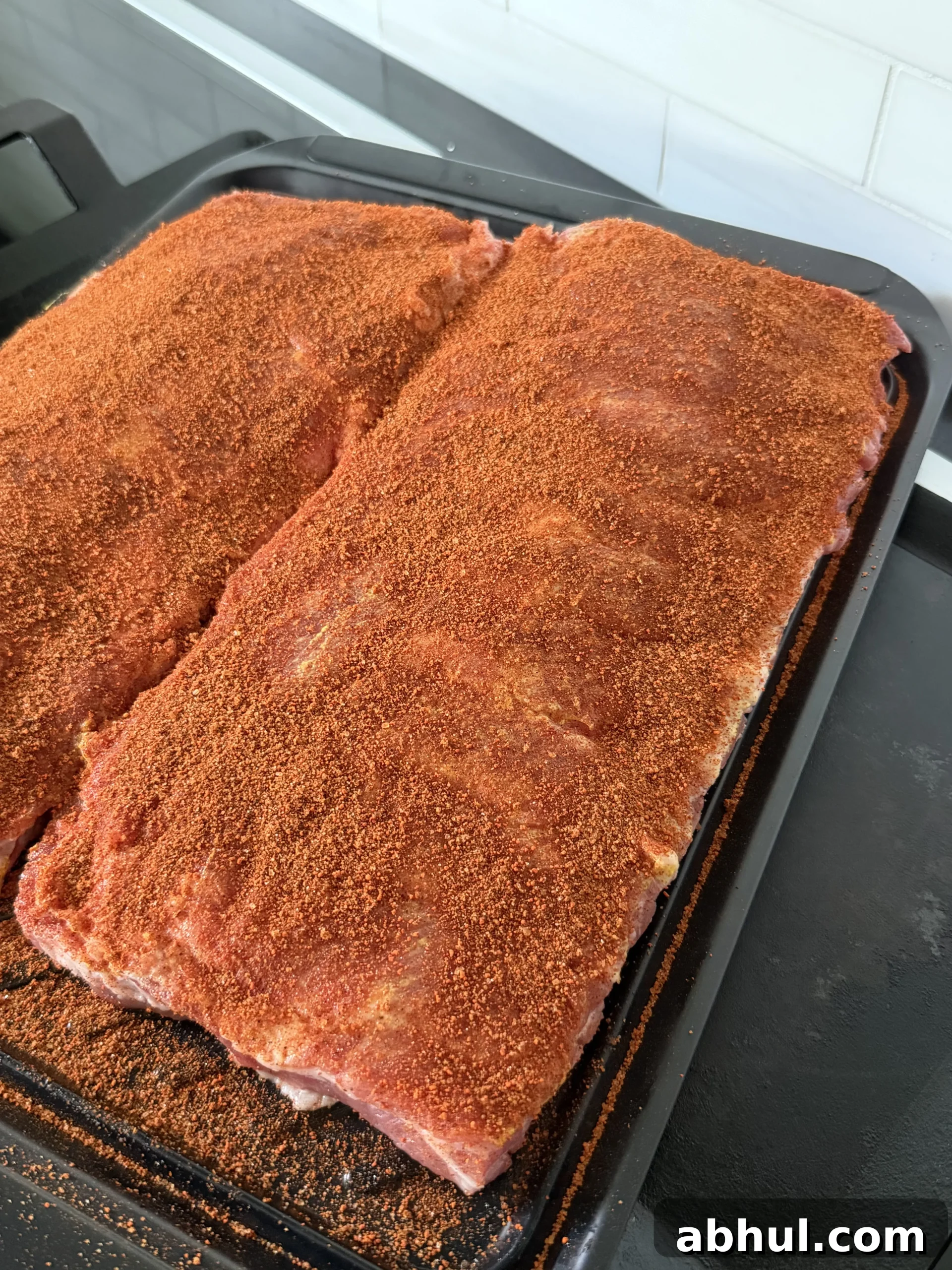 Seasoned pork ribs raw on a black tray ready for the pellet smoker