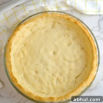 A coconut flour pie crust in a glass dish on a marble countertop.
