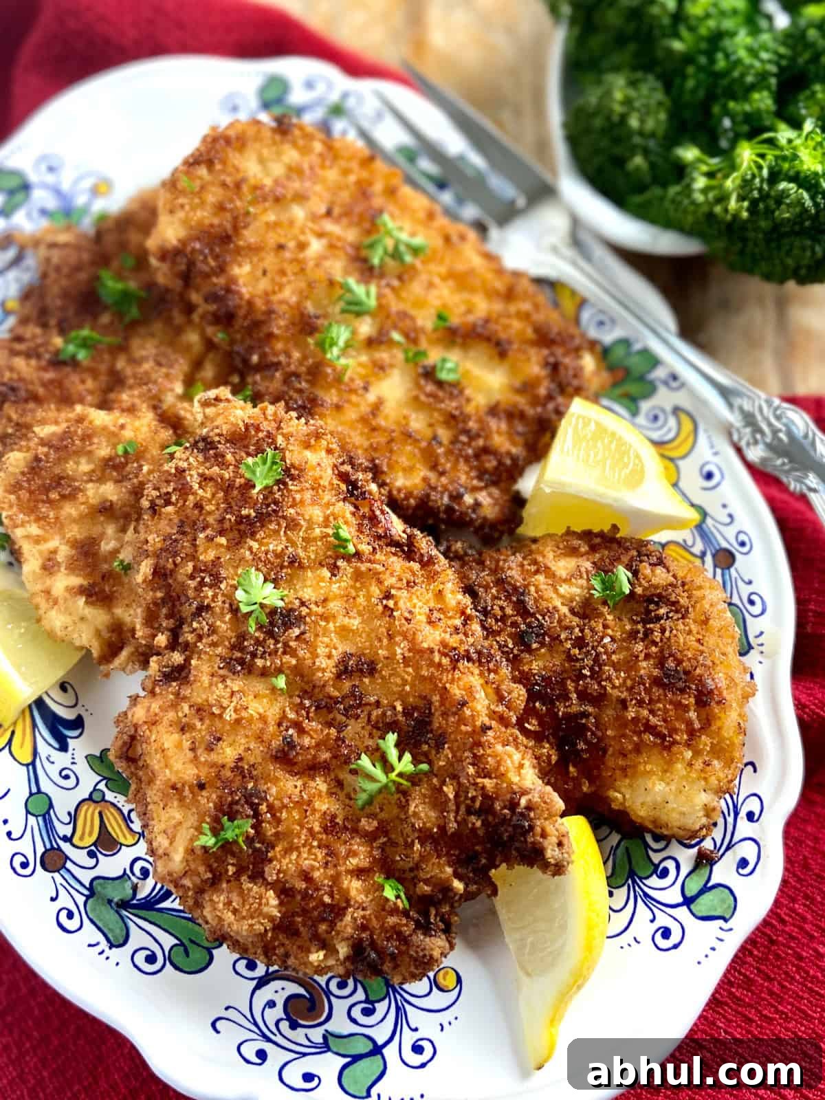 Chicken cutlets on decorative serving platter with lemon wedges.
