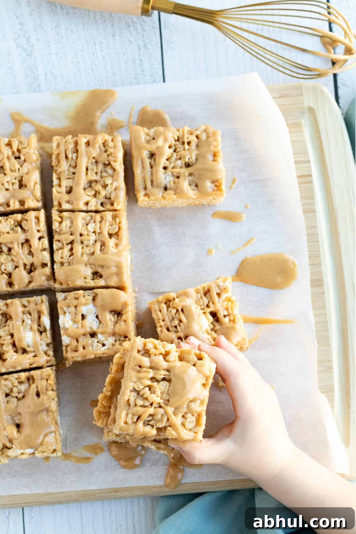 peanut butter rice krispie bars sitting on parchment with a child's hand reaching for a bar