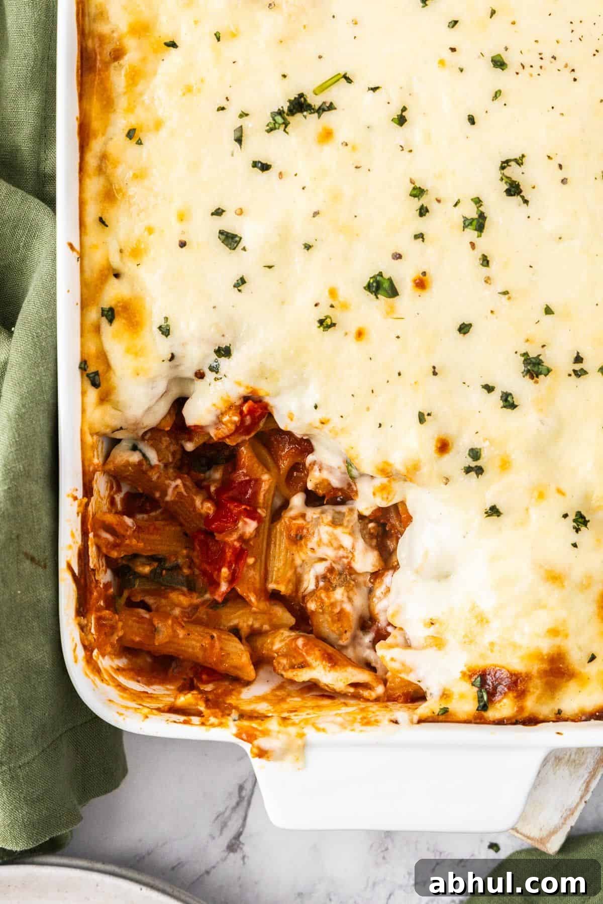 White rectangular dish of Mediterranean Sausage Pasta Bake, topped with a sprinkling of fresh parsley, with a scoop removed.