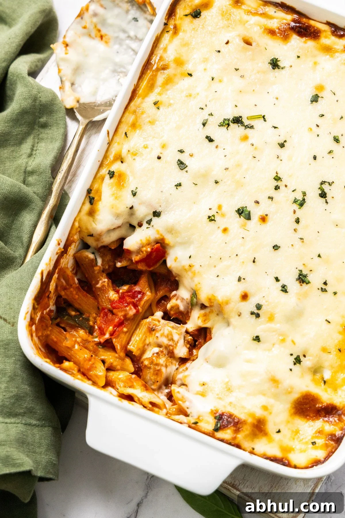 White rectangular dish of Mediterranean Sausage Pasta Bake, topped with a sprinkling of fresh parsley, with a scoop removed.
