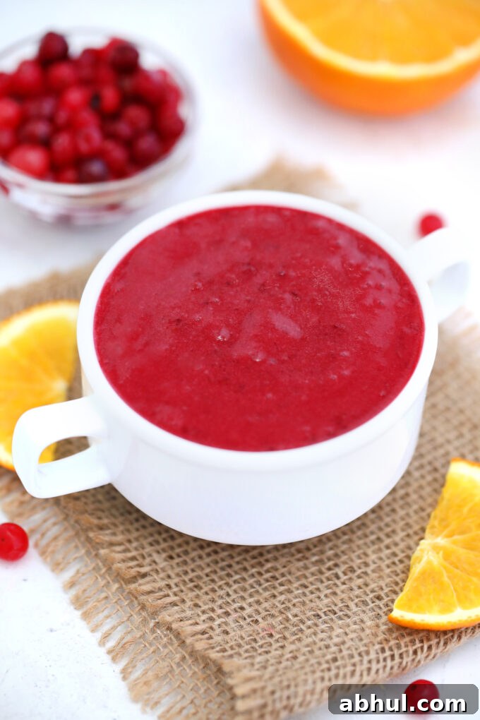 a bowl of cranberry sauce with fresh cranberries and an orange in the background