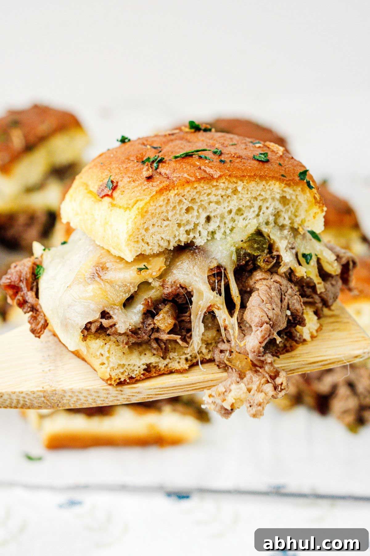 Philly cheesesteak slider on a wooden spatula raised to the camera.