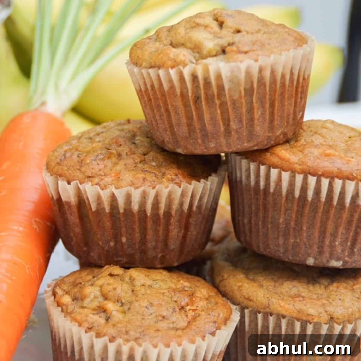 Stack of banana carrot muffins with a carrot on the side.