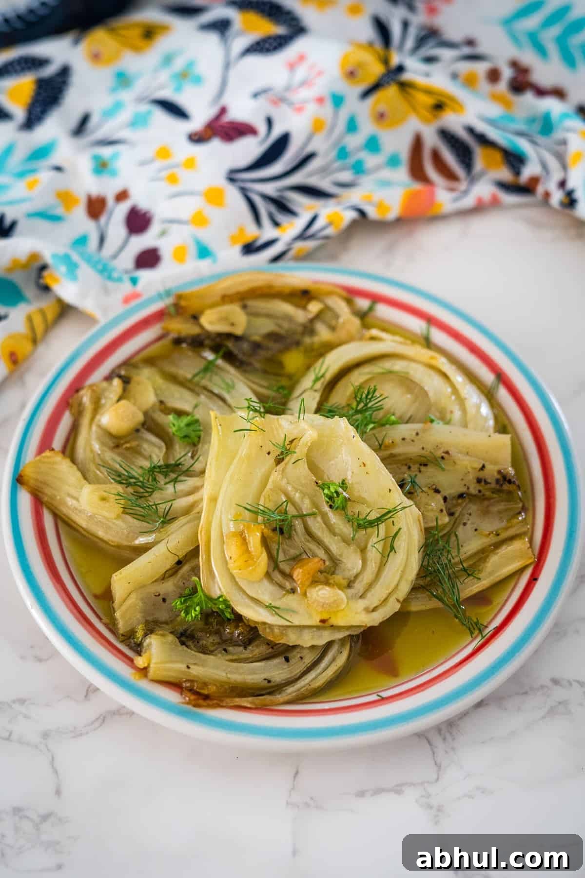 A plate of braised artichokes garnished with fennel confit, served on a colorful striped plate with a patterned napkin on the side.