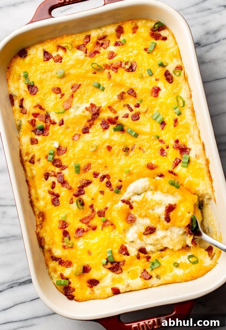 a baking dish with cheesy loaded mashed potato casserole and a serving spoon