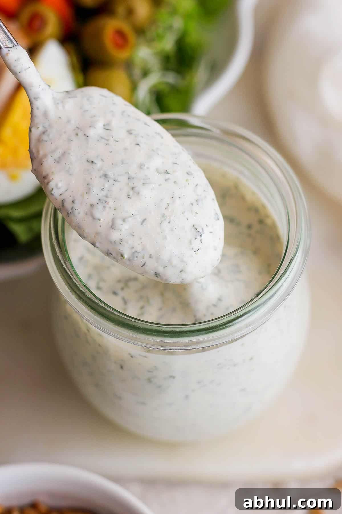 Homemade Herb Ranch Dressing Recipe for Fresh Flavor 5 A spoon with ranch dressing on it hovering over a mason jar.