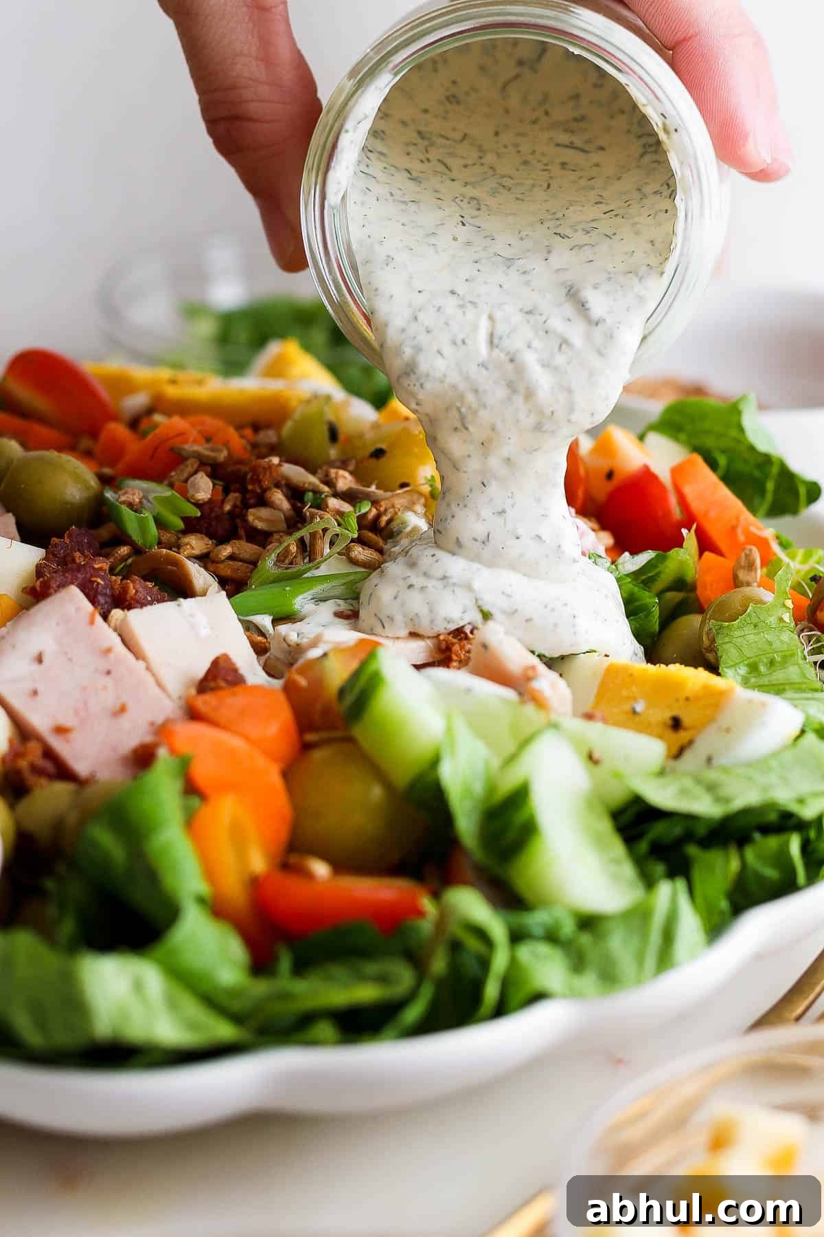 Homemade Herb Ranch Dressing Recipe for Fresh Flavor 6 A hand pouring a jar of ranch dressing over a chef salad.