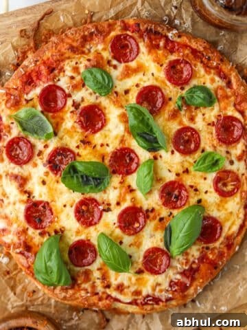 A pizza on parchment paper, topped with pepperoni, cheese, and fresh basil.
