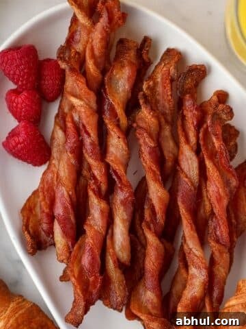 A platter full of twisted bacon/bacon twists, garnished with fresh raspberries.