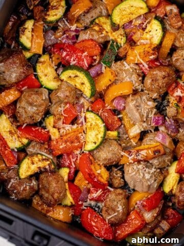 Cooked sausage pieces and vegetables in an air fryer basket.
