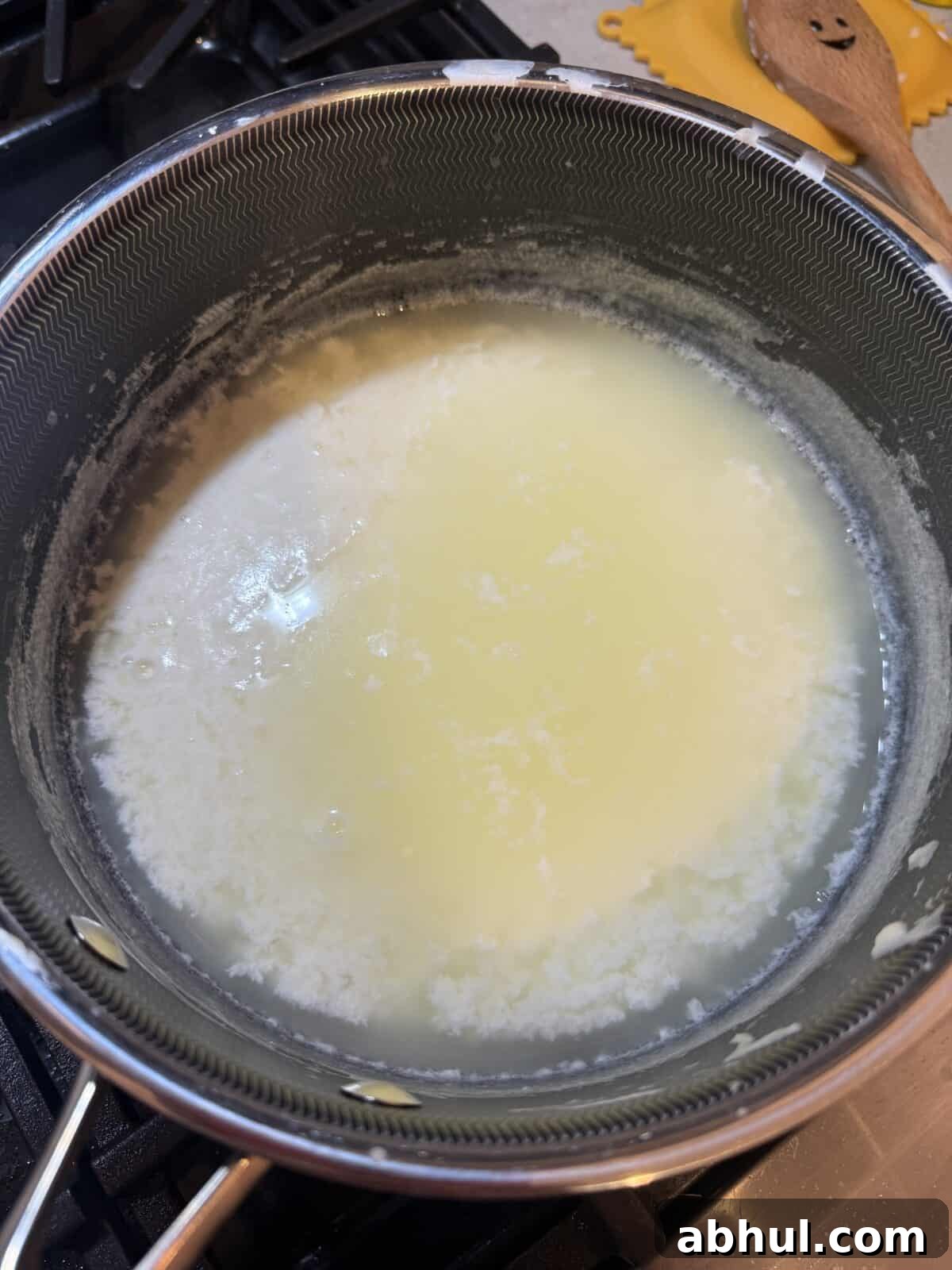 A saucepan on a stove contains curdled milk, with white curds separating from the yellowish whey during the process of making homemade cheese or ricotta. A wooden spoon and silicone trivet are nearby.