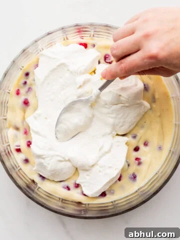 Spreading whipped cream over pastry cream and berries in a bowl to make trifle.