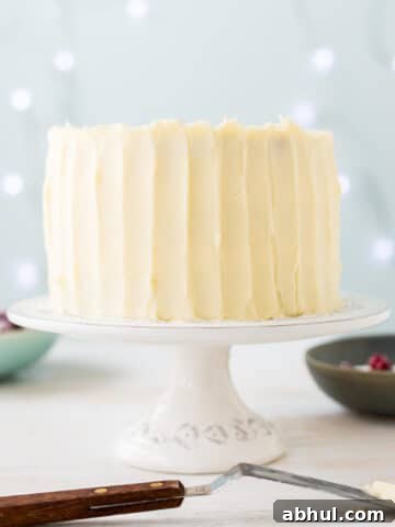 Thick cream cheese frosting on a layer cake, spread with an offset spatula to create vertical streaks on the surface of the frosting.