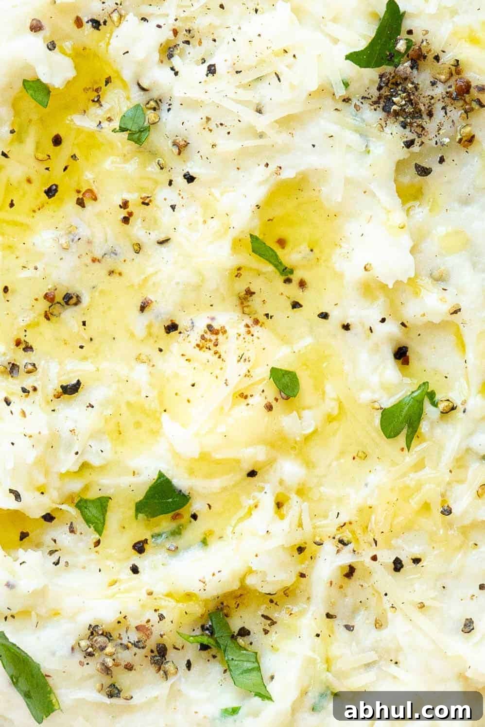 A close up of a bowl of mashed potatoes with parmesan, butter, herbs, and pepper.