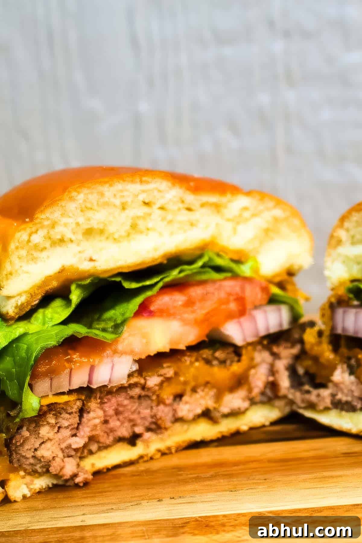 a smoked hamburger that's been cut in half, showing the inside layers of bun, ground beef, red onion, tomato, and lettuce