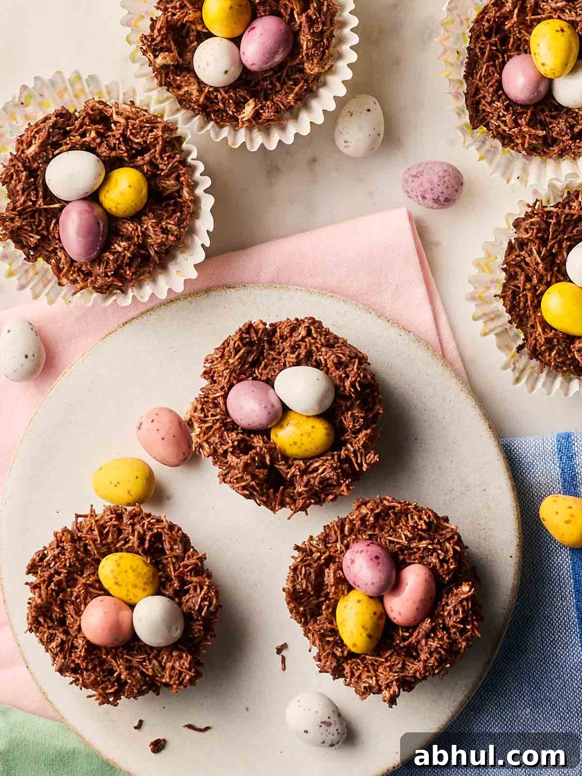A batch of chocolate Easter Nests with mini eggs on top on a table, with scattered mini eggs.