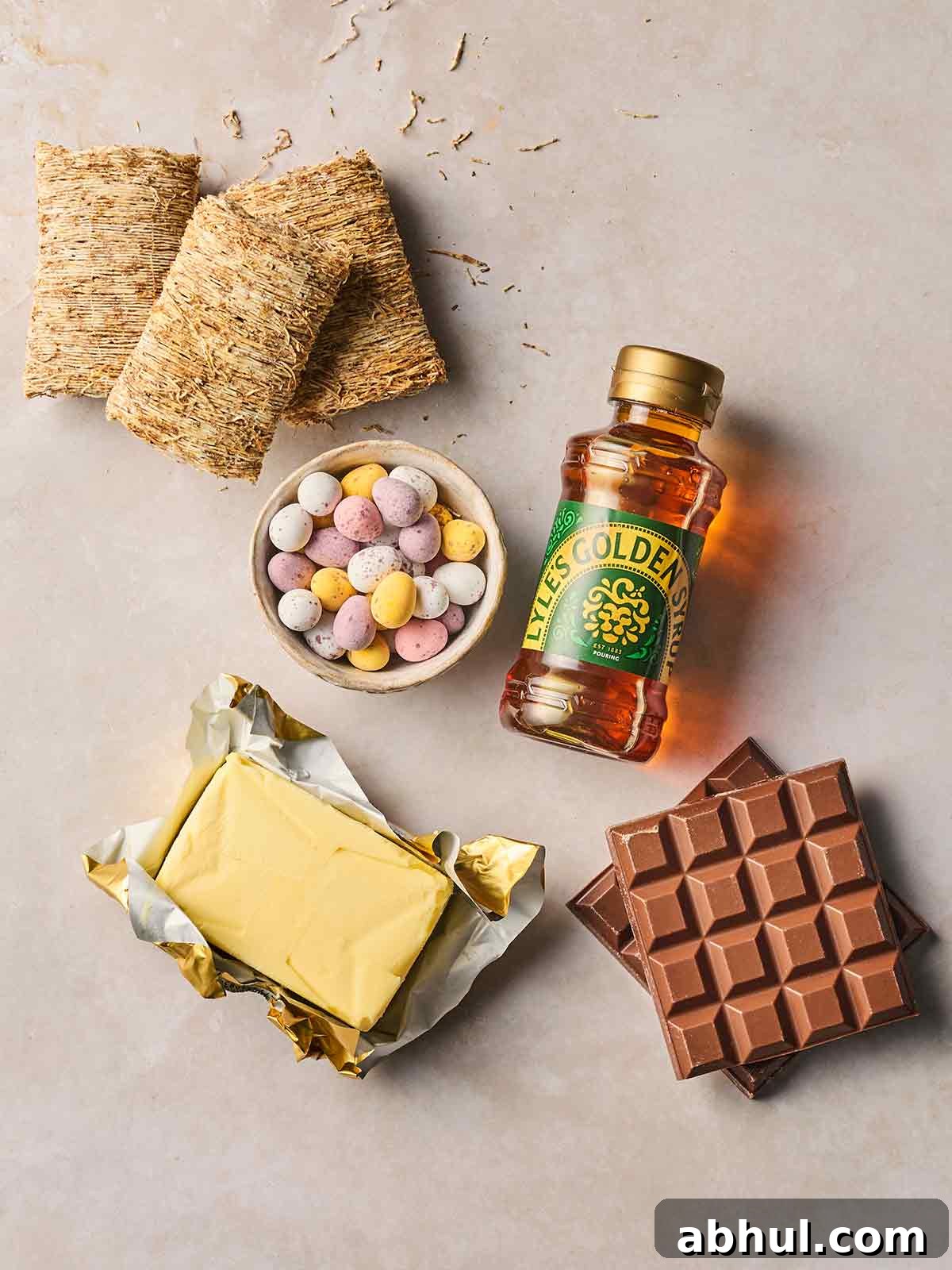 The ingredients for making chocolatey Easter Nests laid out on a white counter, including shredded wheat, golden syrup, mini eggs, butter and chocolate.