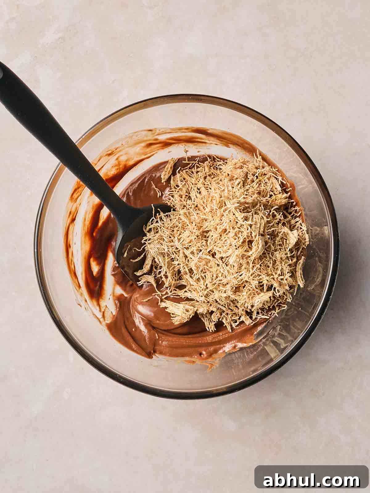 Broken up shredded wheat in a bowl with melted chocolate, being mixed together with a spoon.