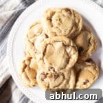 A pile of chubby chewy chocolate chip cookies on a white serving plate.